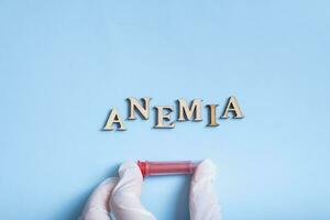 Anemia text with container for blood analysis in gloved hand flat lay, top view photo