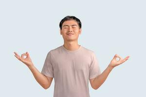 Happy smiling young man standing with closed eyes, having relaxation while meditating isolated on white background. Guy holds hands in yoga gesture, relaxing meditating, and trying to calm down. photo