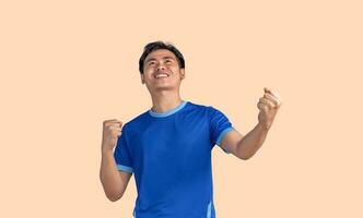 Young man with arms raised in celebration isolated on yellow background. Excited man celebrating success with two fists in air, happiness, positive emotion and feeling. I've done it. facial expression photo