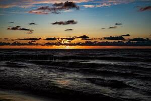 vistoso puesta de sol terminado el polaco báltico mar con oscuro cielo nubes y rompeolas foto