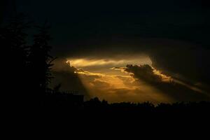 oscuro denso cielo y rayos de calentar naranja ligero consiguiendo fuera de el nubes foto