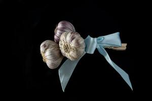 natural cabezas de ajo en un negro antecedentes con el asociado azul cinta foto