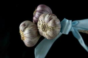 natural cabezas de ajo en un negro antecedentes con el asociado azul cinta foto