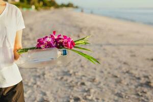 Woman hand holding orchid flowers and bottle of water on the beach. photo