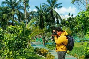Medan, Indonesia, february 2023 - a photographer takes a picture with a camera in a park.  a man in a yellow jacket with a backpack is shooting flowers with his camera. photo