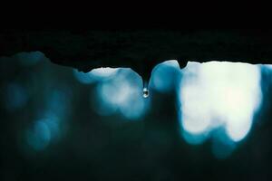 Small water drop with reflection of a forest on icicle formed on the edge of the wall window with visible blurred forest on the background in evening twilight photo