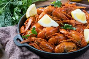 cooked crawfish in black saucepan with lemons and spices on wooden background photo