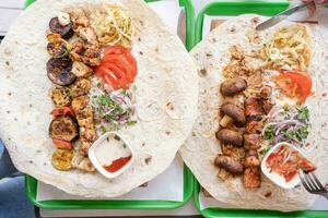 Grilled kebab with pita bread and vegetables on tray in summer fast food street cafe, top view photo