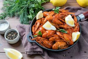 cooked crawfish in black saucepan with lemons and spices on wooden background photo