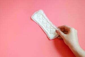 mano sostiene sanitario almohadilla. menstrual concepto en rosado antecedentes. foto