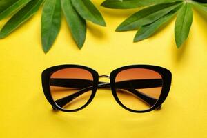 Sunglasses and green leaves on yellow background. photo