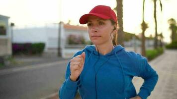 mujer con auriculares carreras abajo el calle a lo largo el palma avenida a puesta de sol. sano activo estilo de vida. lento movimiento video