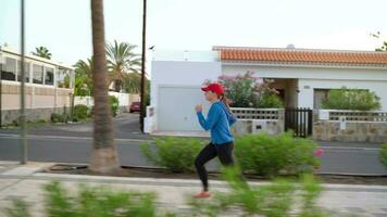 donna con cuffie corre giù il strada lungo il palma viale a tramonto. salutare attivo stile di vita. lento movimento video