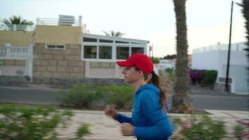 mulher com fones de ouvido corre baixa a rua ao longo a Palma Avenida às pôr do sol. saudável ativo estilo de vida. lento movimento video
