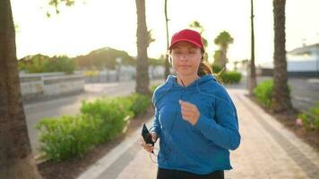 donna con cuffie corre giù il strada lungo il palma viale a tramonto. salutare attivo stile di vita. lento movimento video