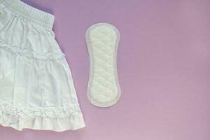White skirt and woman sanitary pad on violet background. Female menstruation cycle period. Hygiene concept. Linen and health protection idea. Copy space photo