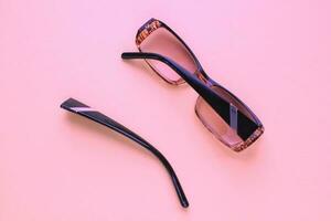 Old broken eyeglasses with damaged legs on pink background. Poor eyesight. Reuse and repair concept. Idea of health. Failure optic eyewear. Breakage of vision correction glasses. Close up, flat lay photo
