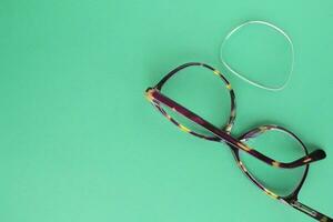 Old broken eyeglasses with damaged lens on green background. Poor eyesight. Reuse and repair concept. Idea of health. Failure optic eyewear. Breakage of vision correction glasses. Close up, flat lay photo