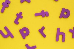 Purple alphabet letters on yellow background. World Dyslexia Day concept. Solving the educational problem of reading. Medical and mental health awareness. Logopedy, psychology, learning lessons photo