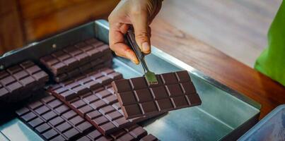 mano de sirvienta usando pinzas caseras barra de chocolate negro fresco. una barra de chocolate de primer plano y un fondo de cacao foto