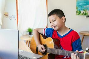 la historia de un niño mirando una computadora portátil mientras se prepara para practicar tocar la guitarra en casa. los chicos toman clases de guitarra clásica en línea. foto