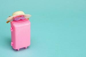 toy suitcase with sunglasses and a hat on a light turquoise background with copy space, travel content photo