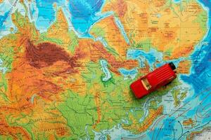 juguete rojo coche en un físico mapa de el mundo viajes desde Europa hacia Rusia foto