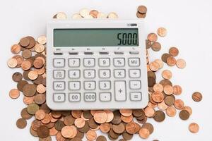 white calculator on a pile of small coins with the dialed number 5000 photo