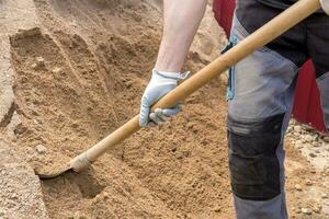 man takes a shovel of sand from an embankment photo