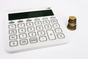 stack of coins next to a calculator on a white background photo