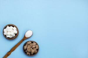 white and brown cane sugar sand and refined sugar in a wooden bowl on a blue background with copy space photo