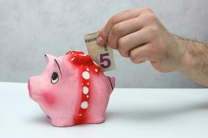 man's hand puts a banknote of 5 dollars in a piggy bank photo