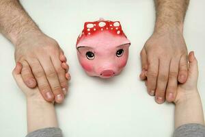 kid and father hold hands, piggy bank between them photo