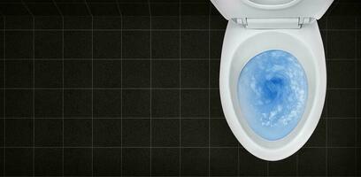 Top view of toilet bowl, blue detergent flushing in it photo