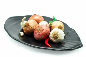 Group of fresh garlic, onions, red and green chilis on black plate over white background photo