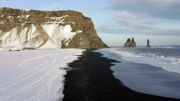 Basso volo al di sopra di il nero sabbia spiaggia di meridionale Islanda coperto nel neve video