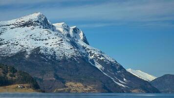 fiordo con nieve cubierto montaña en horizonte. el agua brilla en Noruega. paisaje foto