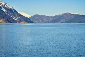 fiordo con nieve cubierto montañas en el horizonte. el agua brilla en Noruega foto