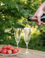 Close-up of a man's hand pouring champagne into a glass in a summer garden photo