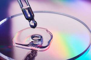 Pipette with sample of cosmetic product in petri dish on holographic background, iridescent highlights, selective focus photo