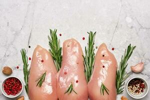 Raw chicken breast fillet with spices and herbs on gray marble background. Preparation for cooking photo