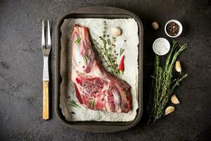 Raw fresh Lamb Meat in baking tray, herbs and fork on black stone background. photo