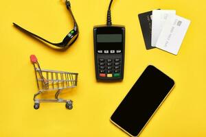 POS payment terminal, watch, bank cards and smartphone on yellow. Minimal financial service concept. Trendy shadows, copy space photo