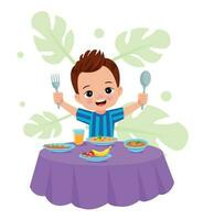 A boy is eating a meal with a fork and spoon. vector