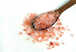 Himalayan pink salt crystals in a wooden spoon on white background. photo