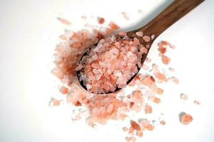 himalaya rosado sal cristales en un de madera cuchara en blanco antecedentes. foto