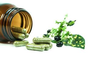 Herbal medicine capsules spilling out of a bottle on white photo