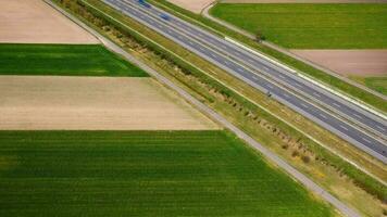 Aerial view of traffic on a highway among green fields. Timelapse video