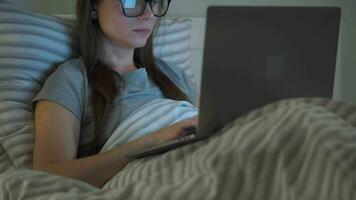 mujer en lentes trabajando en ordenador portátil mientras acostado en cama a noche. móvil adicto o insomnio concepto. video