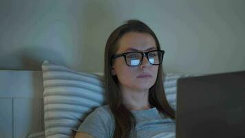 mujer en lentes trabajando en ordenador portátil mientras acostado en cama a noche. móvil adicto o insomnio concepto. video